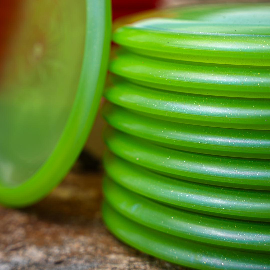 Closeup shot of the green Trash Panda Metal Flake Dune disc golf midrange made from recycled plastic